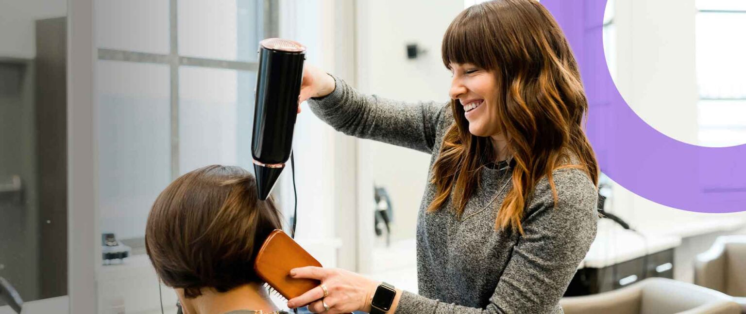 Cabeleireira independente seca e escova o cabelo de uma cliente num salão.